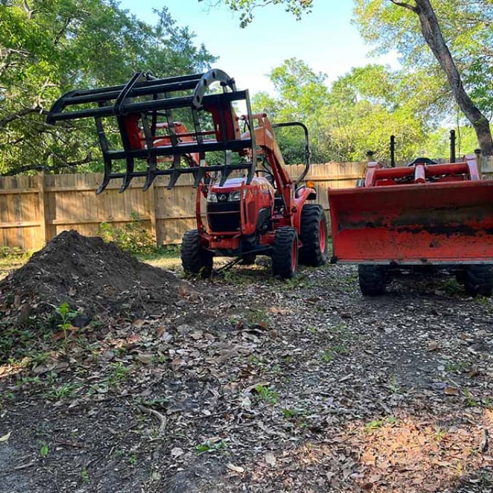 Kubota tractor with grapple attachment clearing debris on a residential demolition job in Mobile, Alabama